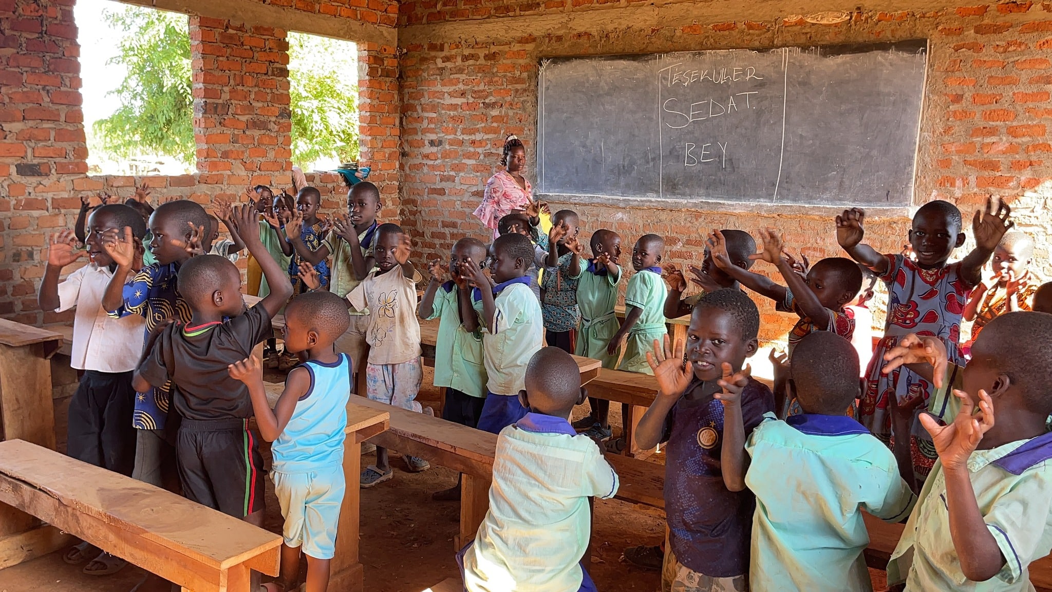 Children sitting in a rustic classroom holding a red balloon.